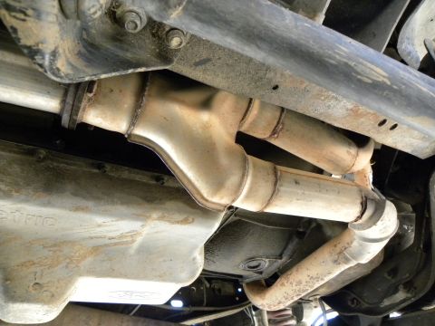 1995 Ford Bronco - Underside view of a vehicle's exhaust system and transmission pan, showing the Y-pipe and catalytic converter.