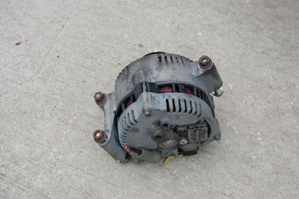Used automotive alternator on concrete showing copper windings and voltage regulator