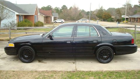 2004 Ford Crown Victoria - A black 2004 Ford Crown Victoria sedan is parked on a driveway, viewed from the side.