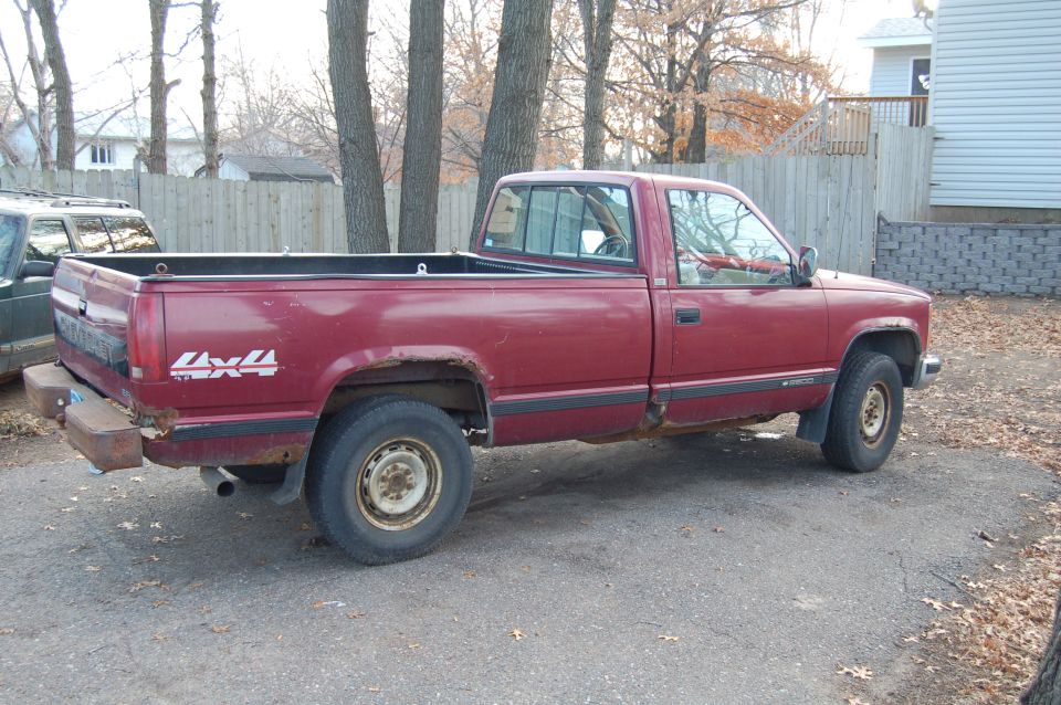 Red pickup truck with 4x4 decal on the bed, showing rust and wear
