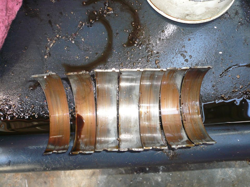 Engine bearings with copper and steel surfaces, some showing wear and oil residue