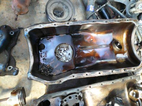 1975 Ford Ranchero - Disassembled engine parts, including an oil pan filled with debris, are laid out on a surface.
