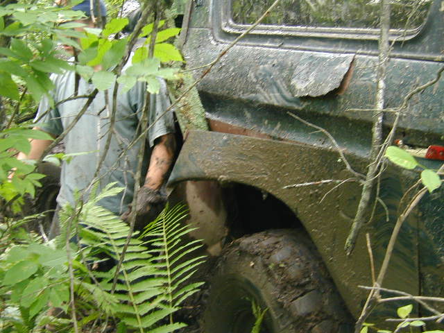 Muddy green off-road vehicle side view, with a person partially visible