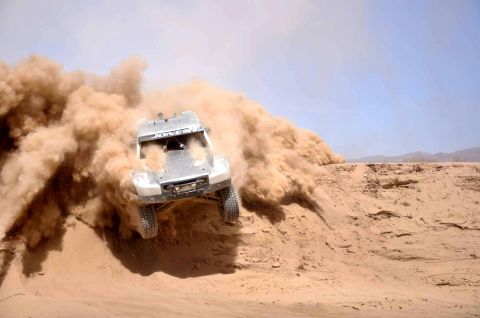1996 Ford Bronco - A custom off-road race truck navigates a dusty desert terrain, sending plumes of sand into the air.