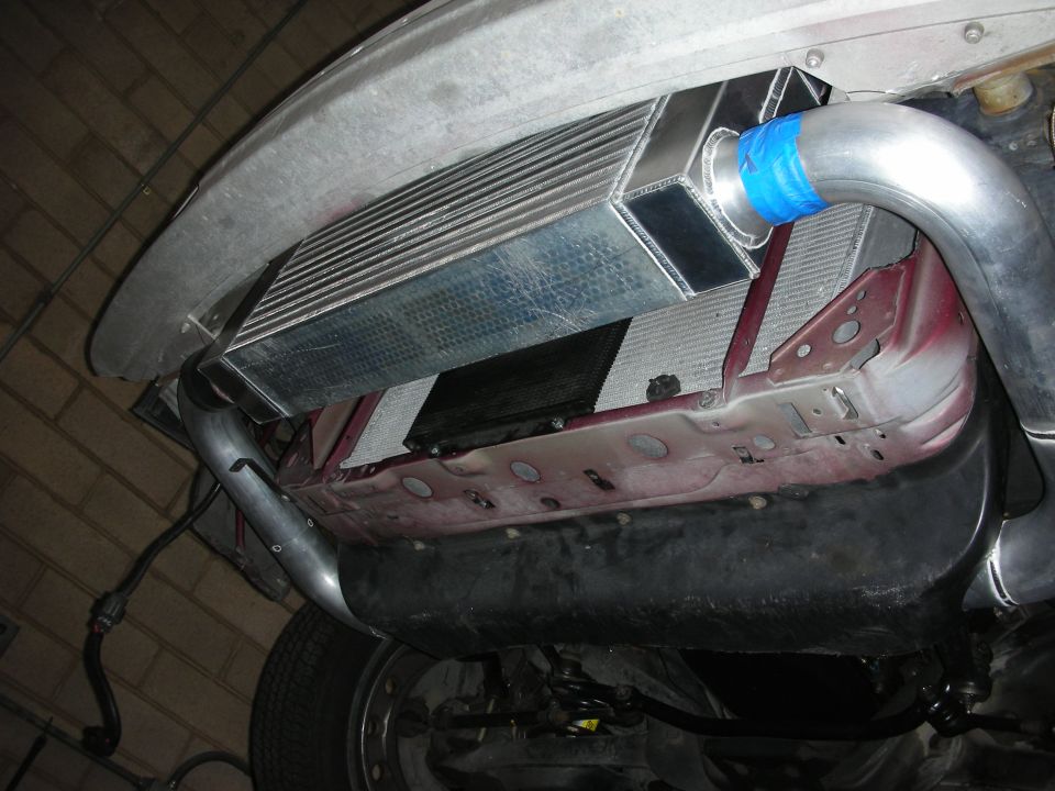 Intercooler and aluminum piping installed under a vehicle, with blue tape on a connection