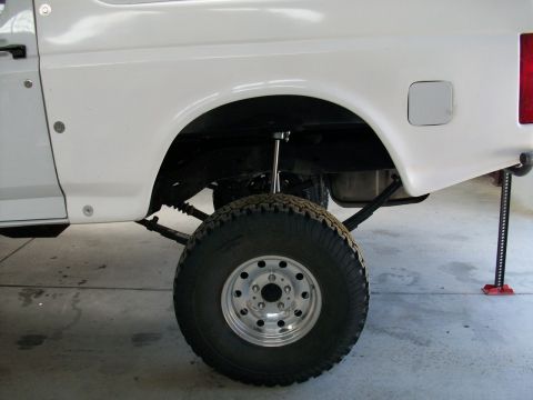 1996 Ford Bronco - Close-up view of the rear suspension and wheel well of a white SUV, with a jack visible on the right.