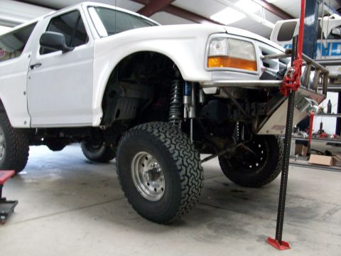1996 Ford Bronco - A white 1996 Ford Bronco is shown in a garage with its front end lifted by a jack.
