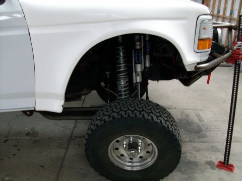 1996 Ford Bronco - Close-up of the front fender and suspension of a white Ford Bronco, showing aftermarket modifications.