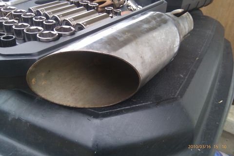 2000 Mercury Grand Marquis - A close-up view of a metal exhaust tip resting on a black surface next to a set of socket wrenches.