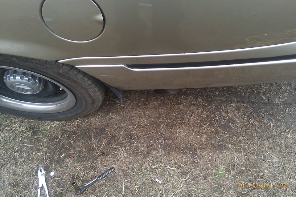 Gold 2000 Mercury Grand Marquis rear quarter panel and wheel, showing a gas cap door and chrome trim