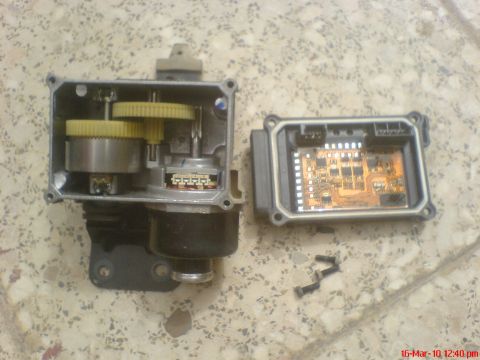 1998 Ford Crown Victoria - The internal components of a cruise control actuator, including gears and a circuit board, are laid out on a speckled surface.