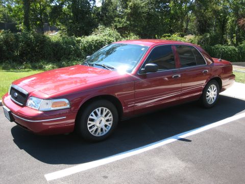 2003 Ford Crown Victoria - This red 2003 Ford Crown Victoria is parked on an asphalt lot with trees in the background.
