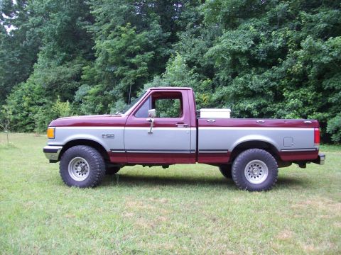 1990 Ford F-150 - This two-tone Ford F-150 pickup truck is shown from the side, parked on a grassy area with a wooded background.