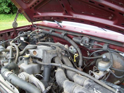 1990 Ford F-150 - The engine bay of a maroon Ford F-150, viewed from above with the hood raised.