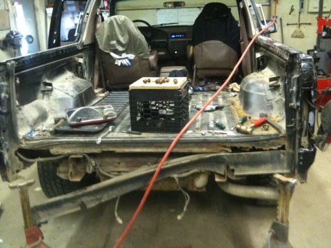 1993 Ford Bronco - The rear of a 1992 Ford Bronco is shown disassembled, with visible rust and tools in the cargo area.