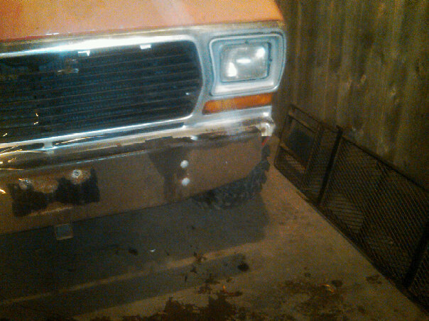 Front of an orange Ford truck with a chrome grille and bumper. Headlight is visible