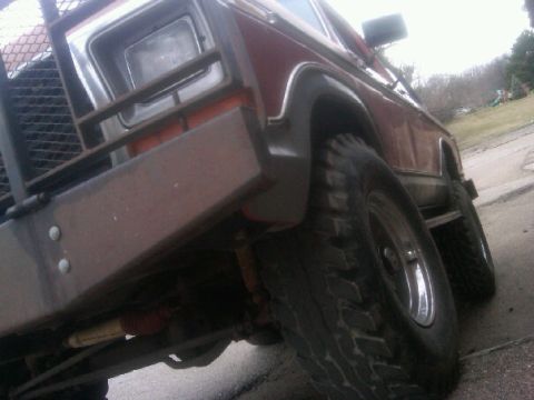 1987 Ford Bronco - A red SUV with a prominent brush guard is viewed from a low angle, highlighting its front tire and fender.