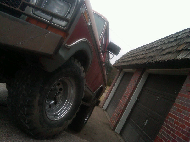 Red SUV with large tires and aftermarket bumper parked next to a garage