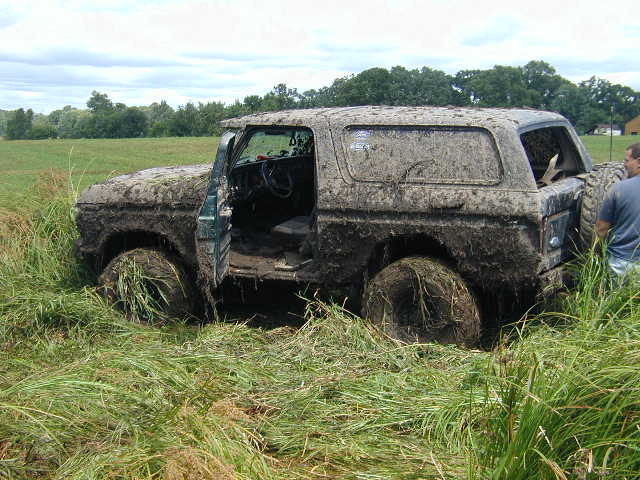 Doorless mud-covered full-size SUV on big mud tires sitting in a grassy field