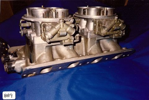 1973 Ford Mustang - A pair of carburetors are mounted on a silver intake manifold, resting on a blue surface.