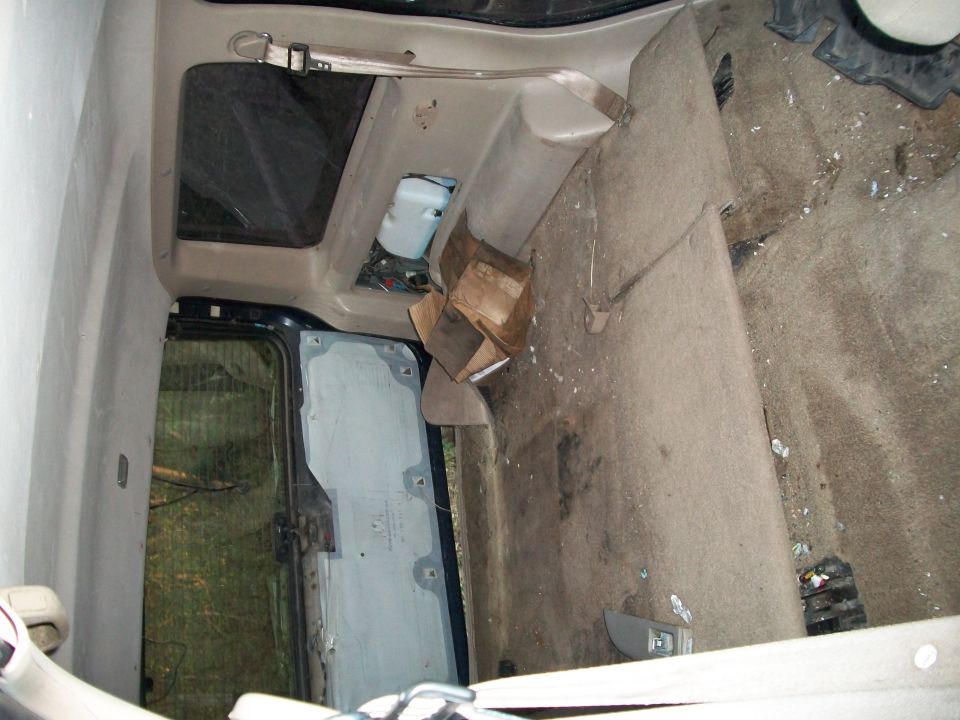 Stripped SUV interior with seats removed, tan carpet, cardboard box, sunroof and open door visible.