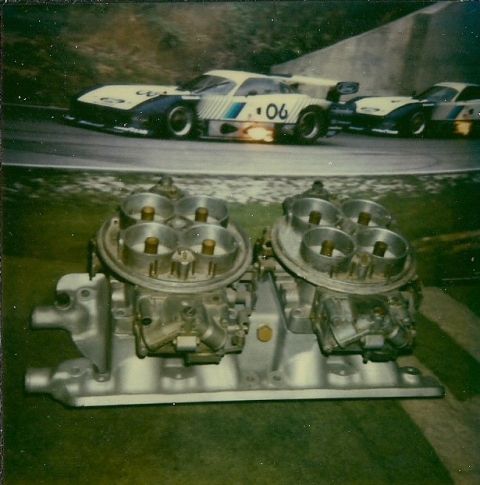 1973 Ford Mustang - Dual carburetors and intake manifold in foreground, race cars on track in background.