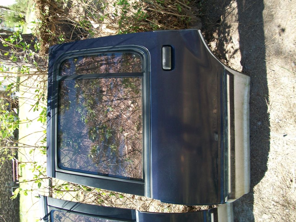 Removed dark blue Ford Explorer rear door with glass, lying outdoors on dirt, photo rotated sideways