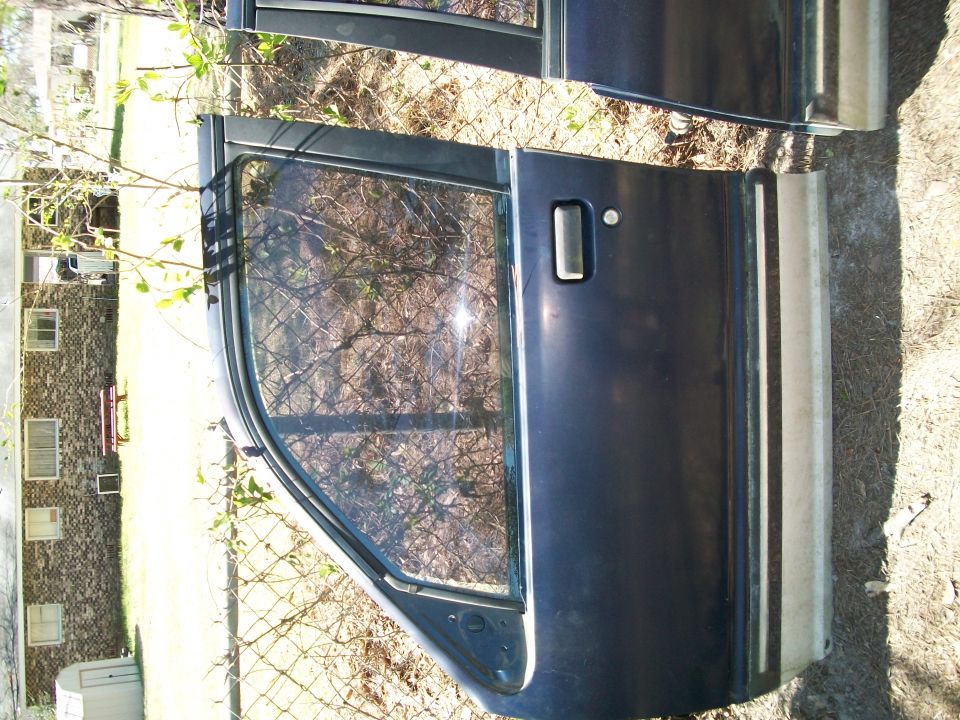Dark removed vehicle door leaning against a fence, rotated view