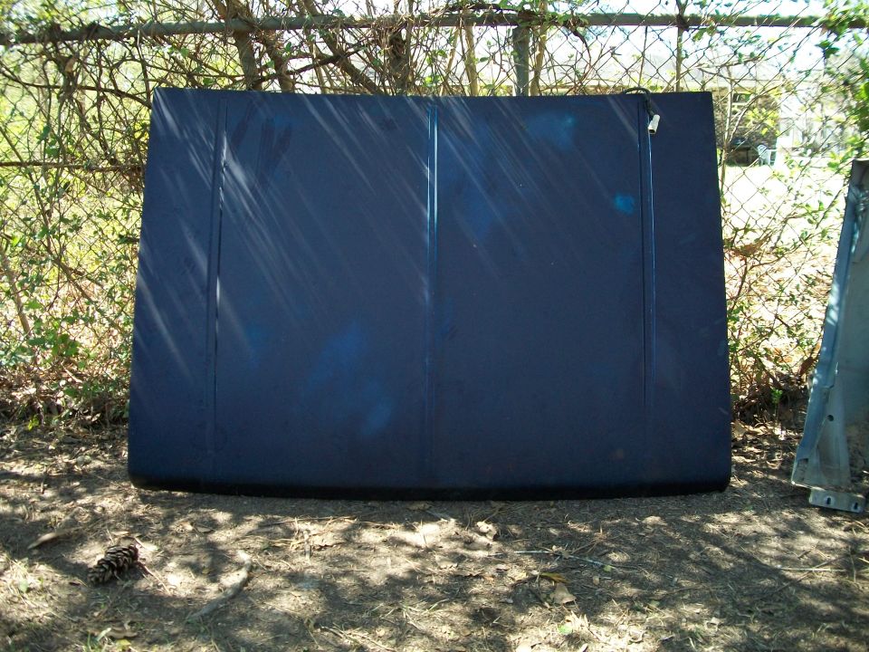 Dark blue vehicle hood leaning against a fence outdoors
