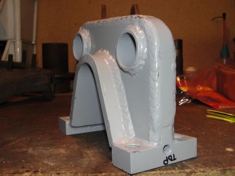 1995 Ford Bronco - A custom-fabricated metal bracket, likely for a vehicle's suspension or drivetrain, sits on a workbench.