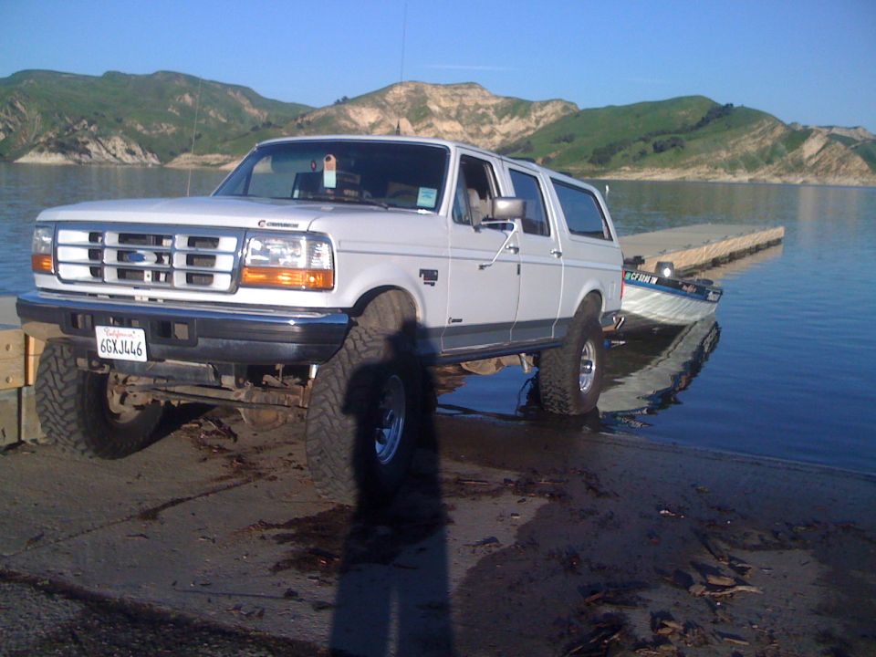 White 1992 Ford Bronco parked on boat ramp with boat trailer in water