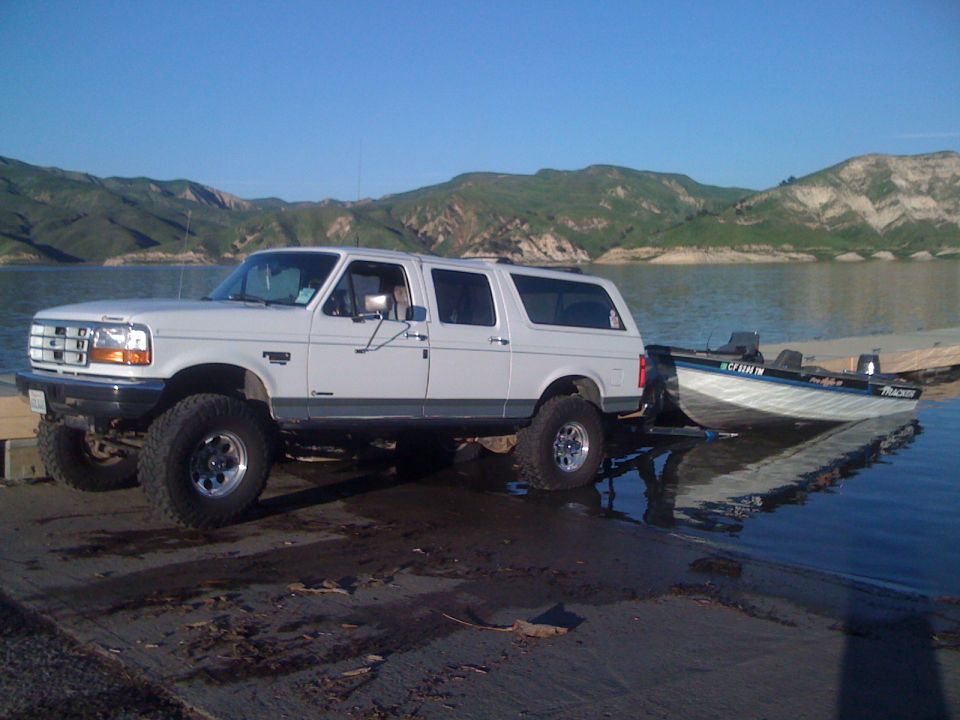 White Ford Bronco pulling a boat trailer into the water at a lake