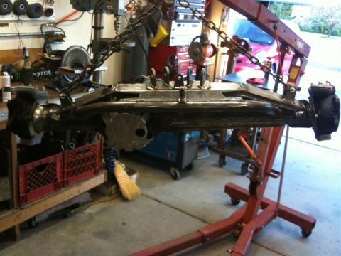 Suzuki Samurai - A vehicle's front axle assembly is suspended by chains and an engine hoist in a workshop setting.