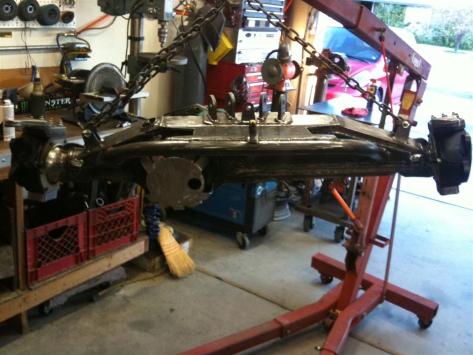 Front axle assembly hanging from engine hoist in a garage
