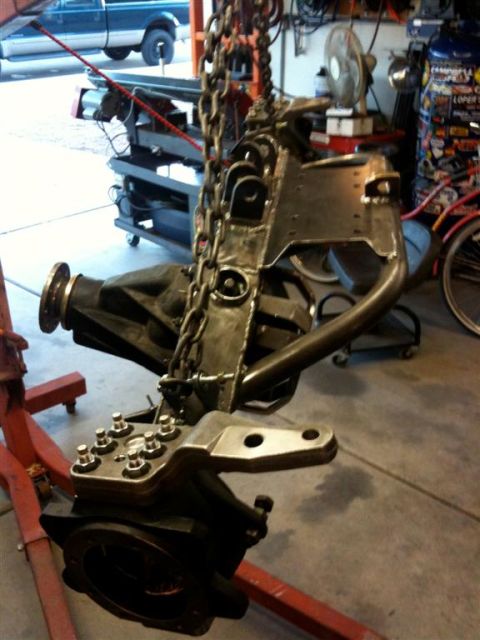 Suzuki Samurai - A custom front axle assembly is being worked on in a garage, with a blue pickup truck visible in the background.