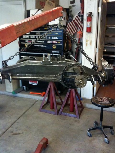 Suzuki Samurai - Front axle assembly, likely from a 4x4 vehicle, is suspended by chains and resting on jack stands in a workshop.