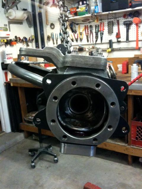 Suzuki Samurai - A cast transfer case or transmission case hanging from a chain hoist in a home shop, viewed straight into the open bellhousing/adapter flan…