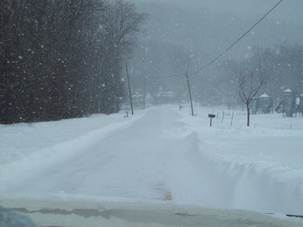 Snowy road with trees and silos in the background
