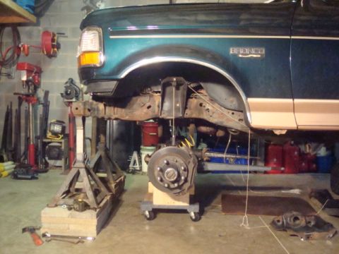 1995 Ford Bronco - Front suspension work on a 1995 Ford Bronco, lifted on jack stands in a garage.