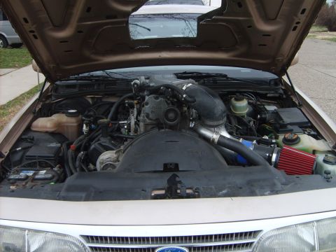1993 Ford Crown Victoria - Engine bay of a tan/gold Ford with the hood raised, showing a V8 engine with a black plastic intake plenum, and an aftermarket cold-air int…