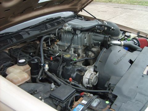 1993 Ford Crown Victoria - Engine bay of a Ford with a V8 engine, showing the intake manifold, alternator, and a red aftermarket cone air filter feeding into a black…