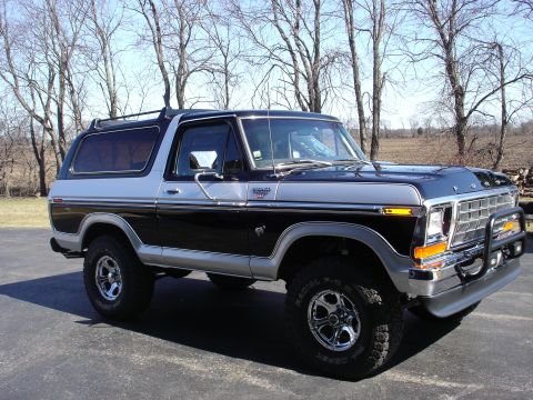 1979 Ford Bronco - This two-tone Ford Bronco sits parked on an asphalt surface with trees in the background.