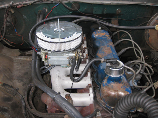 Engine bay with blue valve cover, white intake manifold, carburetor and chrome air cleaner