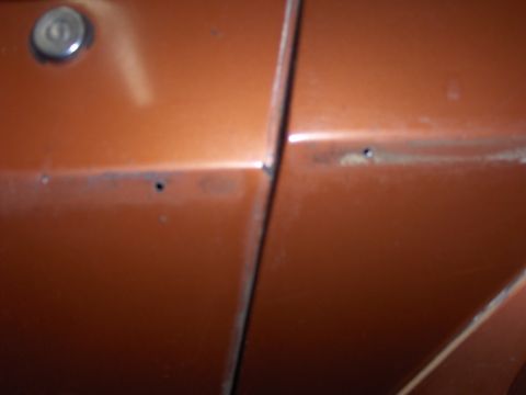 1980 Chevrolet Camaro - Close-up of an orange car's door seam, showing signs of wear and rust.