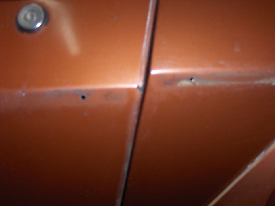 Orange car door seam with rust spots and a keyhole