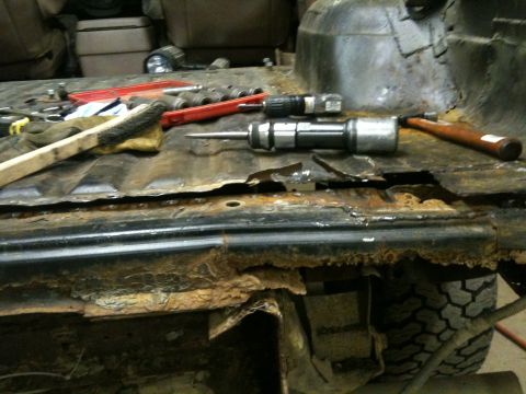 1993 Ford Bronco - Tools are laid out on a severely corroded vehicle floor, indicating repair work.