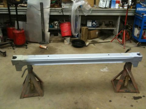 1993 Ford Bronco - A car rocker panel is supported by jack stands in a garage setting with tools and equipment in the background.