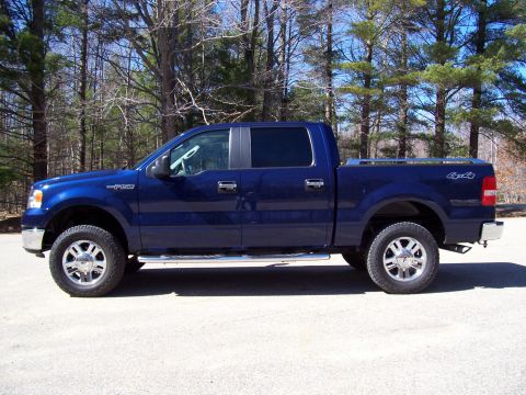 1978 Ford F-150 - This blue pickup truck is parked on a paved surface with trees in the background.