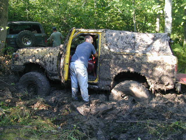 Man reaching into the open cab of a yellow SUV stuck to its axles in deep mud