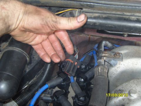 1989 Ford Bronco - Close-up of a hand working on electrical connectors in a vehicle's engine bay.